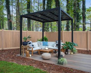 a black pergola on a decking area with cosy seating