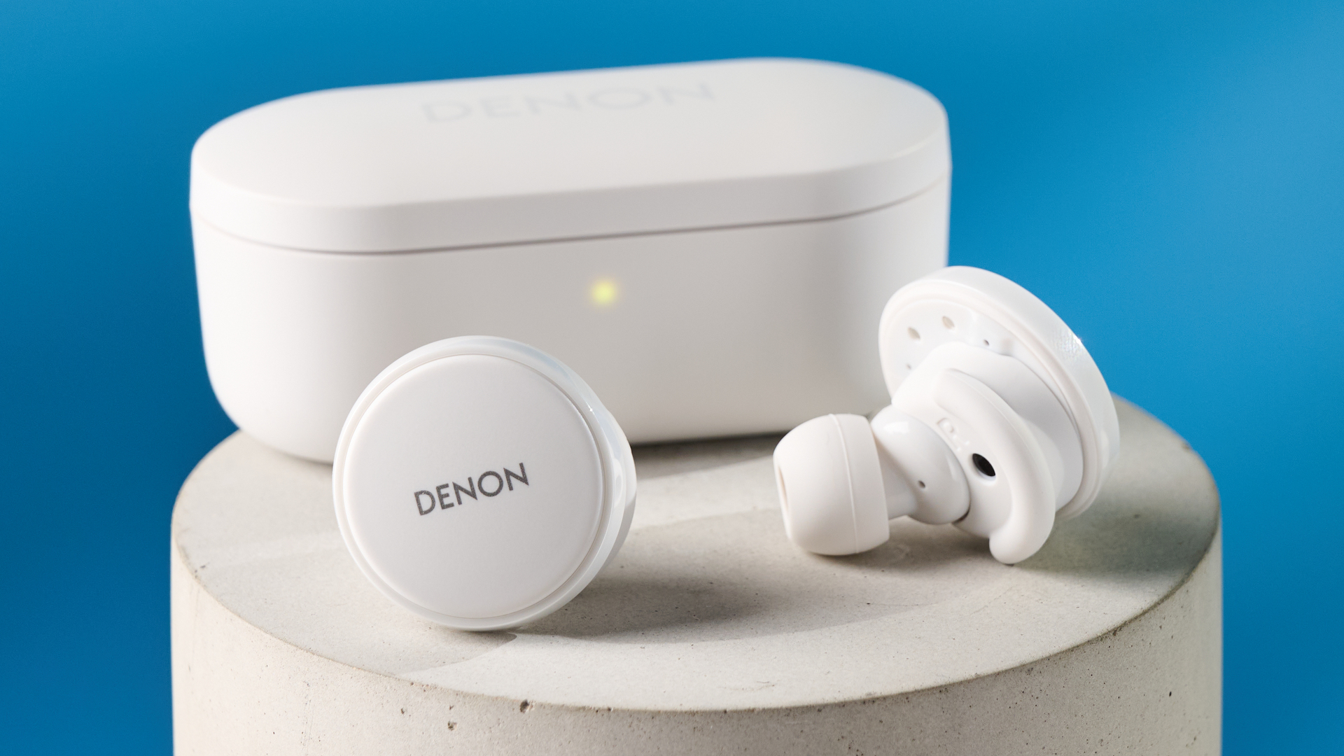 the denon perL Pro wireless earbuds in white, with circular earbud shapes, and a white charging case, photographed against a blue background
