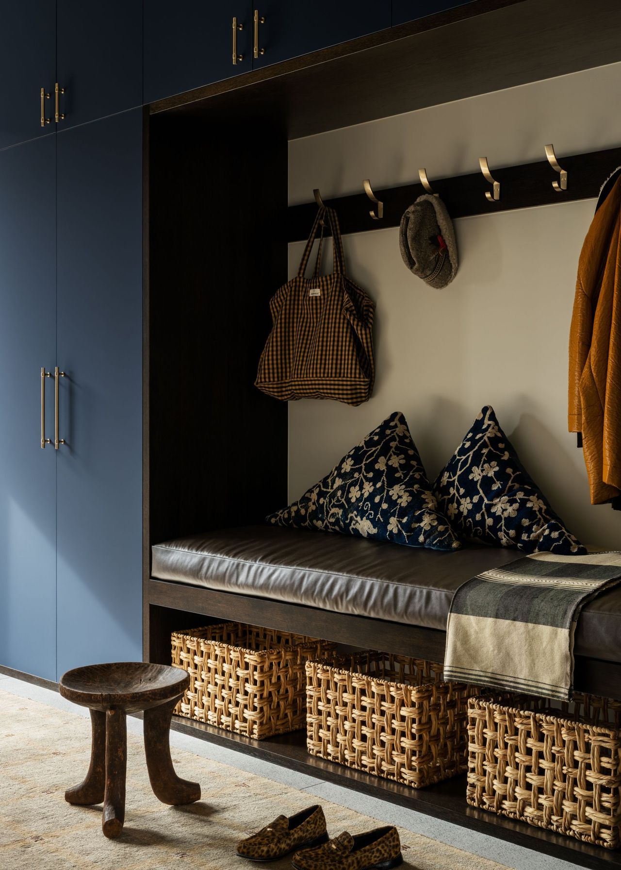 A contemporary mud room with built-in storage, open storage with baskets with built-in bench seating above it and hooks hanging above that with a hat, bag and coat hanging