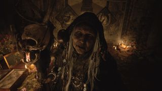 En ældre heks kigger på os omgivet af kranier og okkulte sager i Resident Evil Village