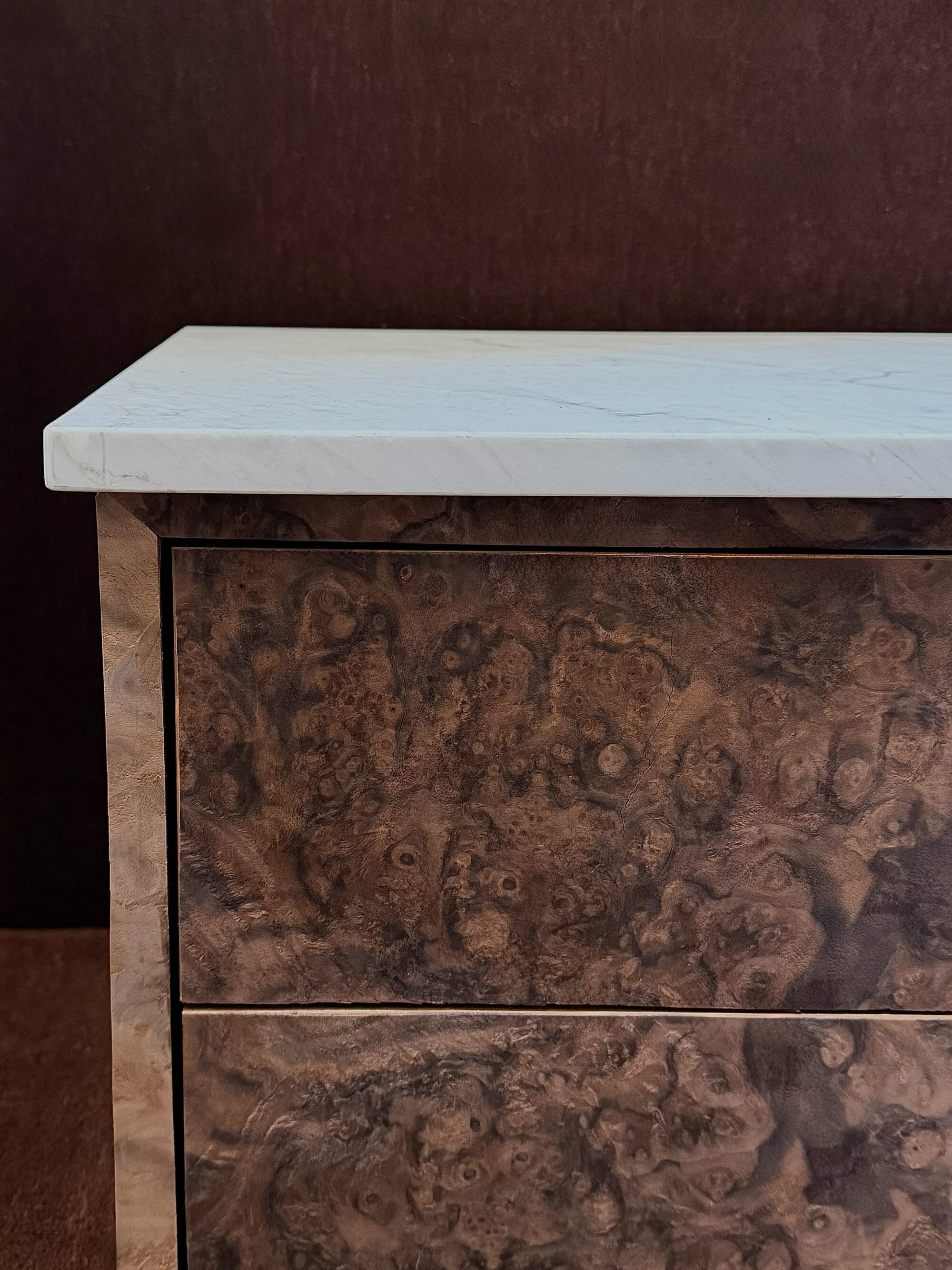 Close-up image of a burl wood nightstand with a white marble top.