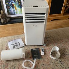 Flat lay of what you get in the box of the Devola DVAC09CW portable air conditioner, including the main unit, exhaust hose, drainage hose, instructions and remote