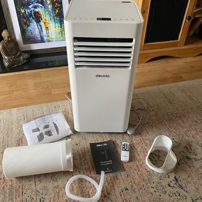 Flat lay of what you get in the box of the Devola DVAC09CW portable air conditioner, including the main unit, exhaust hose, drainage hose, instructions and remote