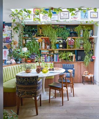 Maximalist kitchen-diner space, bench seating, rounded marble tulip dining table, gallery wall, skylight, plants decorated around the table, wooden flooring