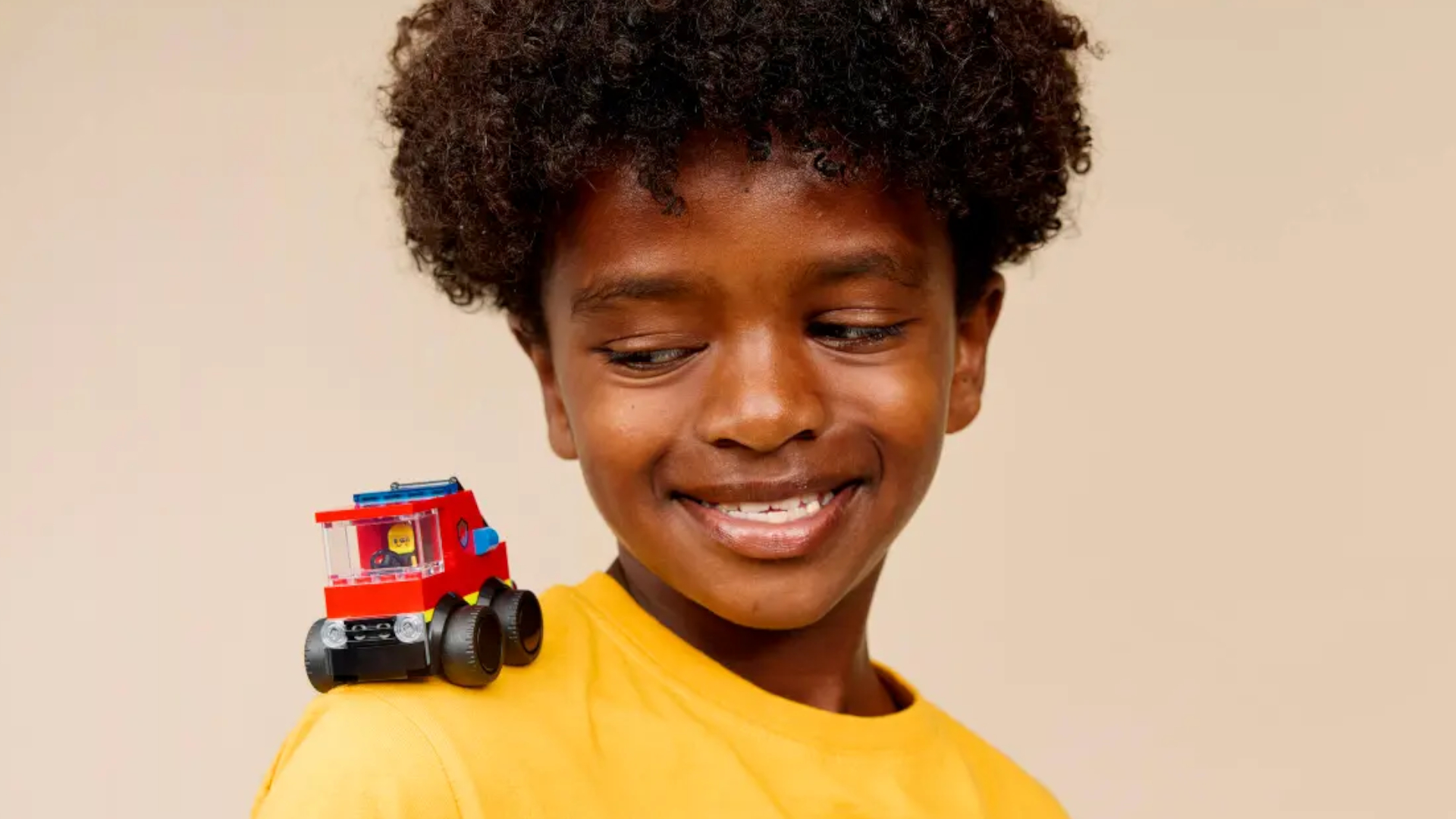 A child smiles with the Lego Rides - Fire Truck on their shoulder
