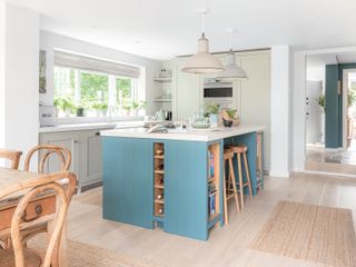 kitchen with blue island and pale cabinets with wooden bar stools