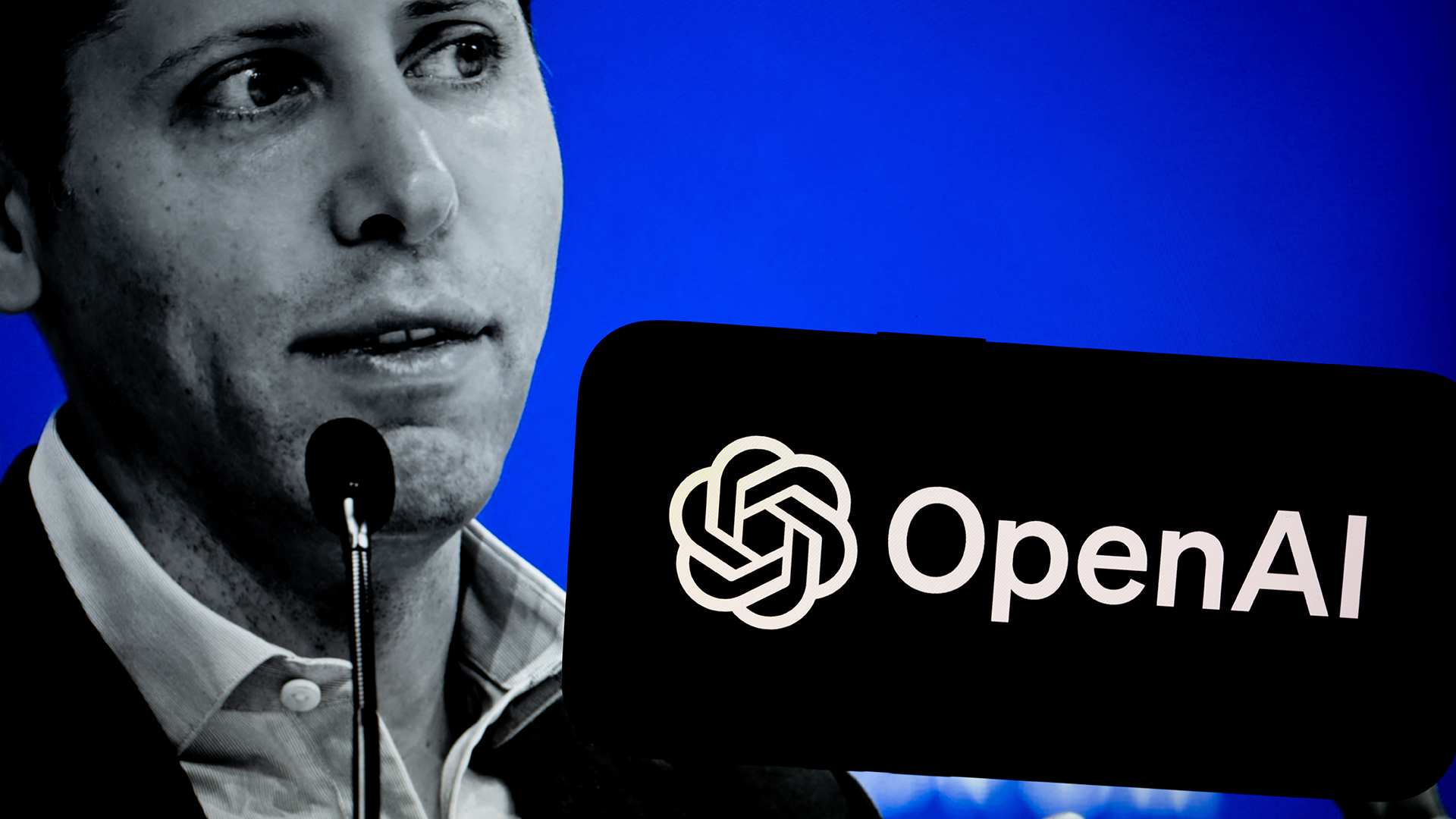 A black and white photo of Sam Altman, CEO at OpenAI, on a blue background with a phone bearing the OpenAI logo held in the foreground.