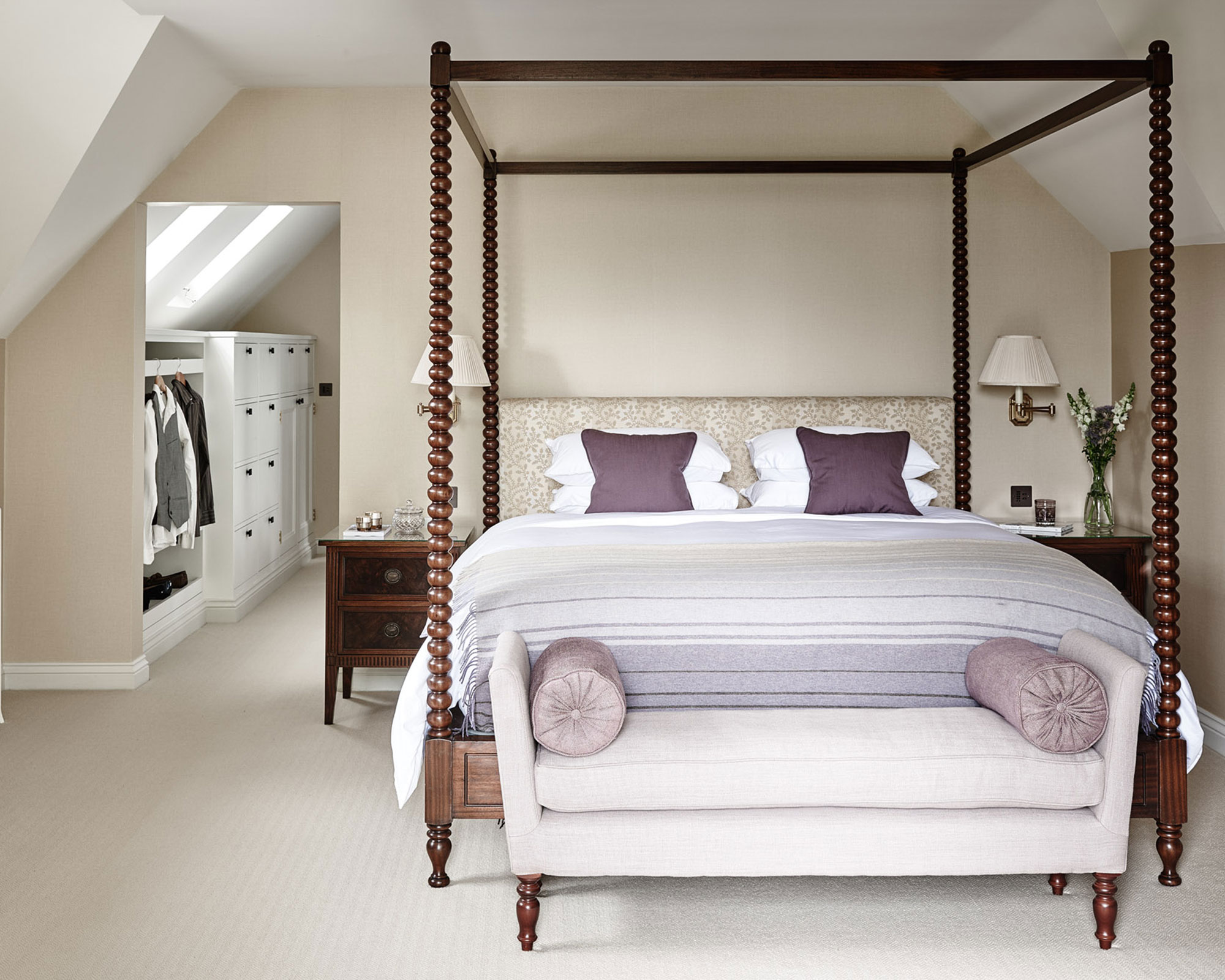Walk-in closet ideas with white storage solutions, shown beyond a taupe colored bedroom with large four poster bed.