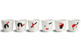 'AXO' tableware collection, by Non Sans Raison. A row of white tumblers with black and red shapes on them.