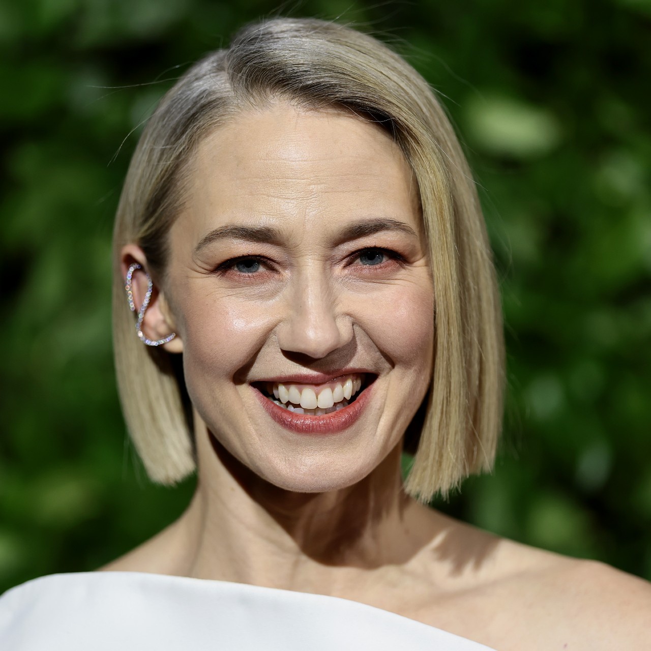 a headshot of a white woman with short hair posing in front of grassy background 