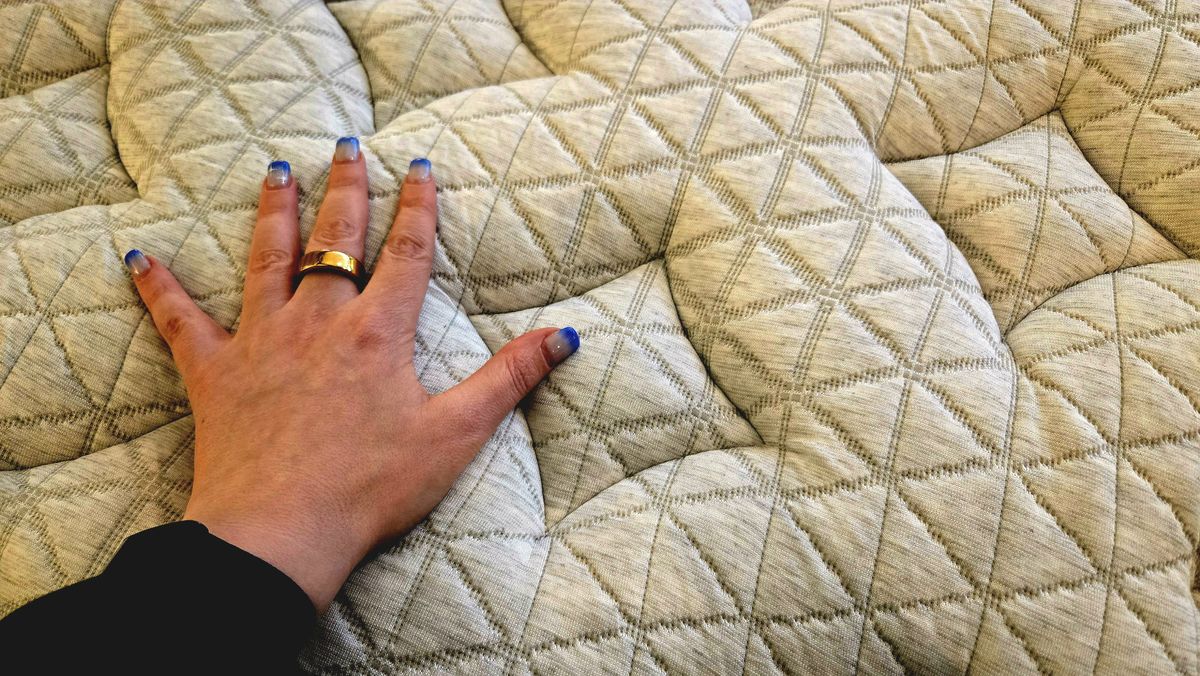 Tester's manicured hand on the cover of the updated Helix Midnight Luxe Mattress with the Tencel cover