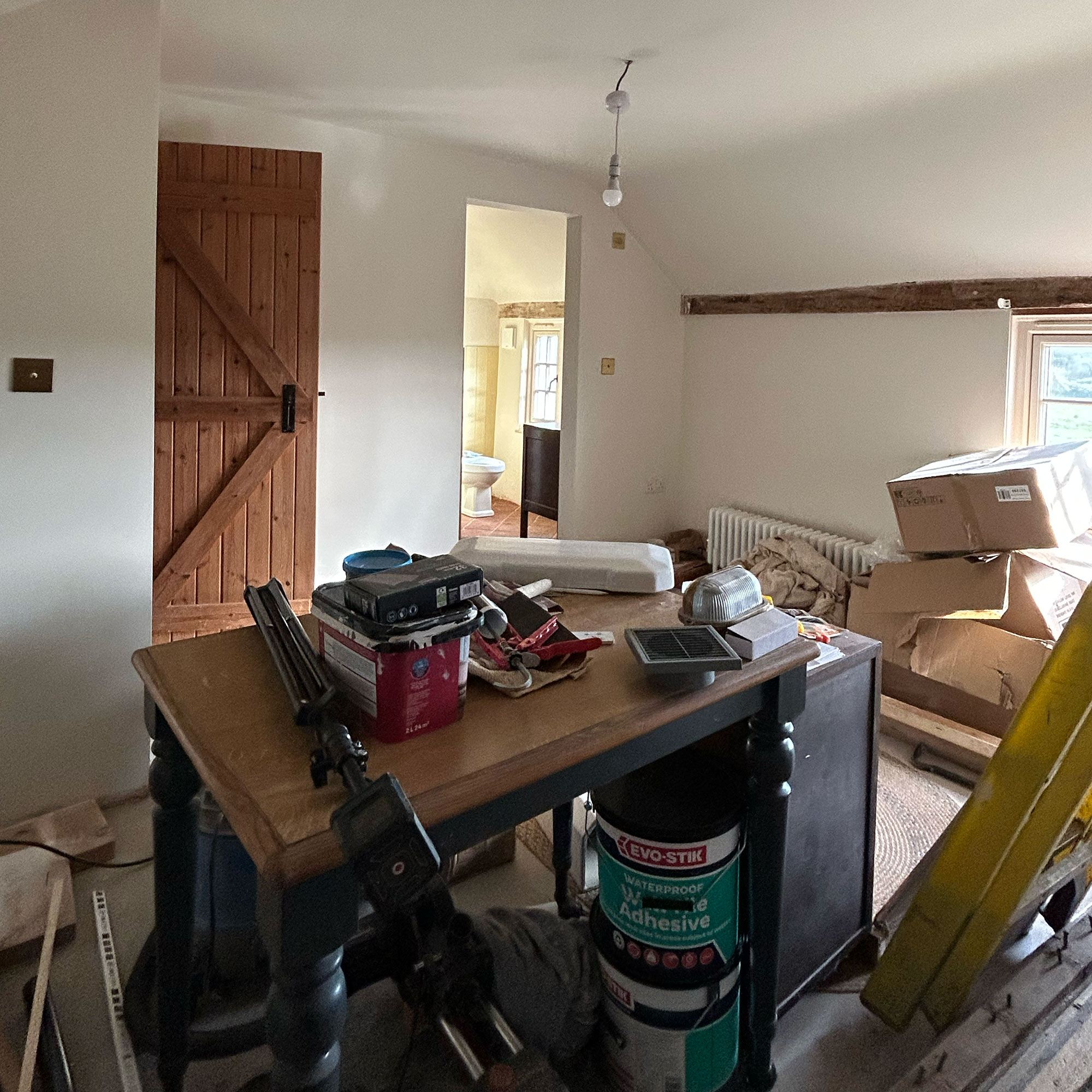 Room mid-renovation with piles of adhesive, tools and cardboard boxes