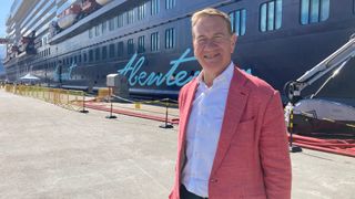 Michael Portillo in a pink jacket standing in front of a huge ship