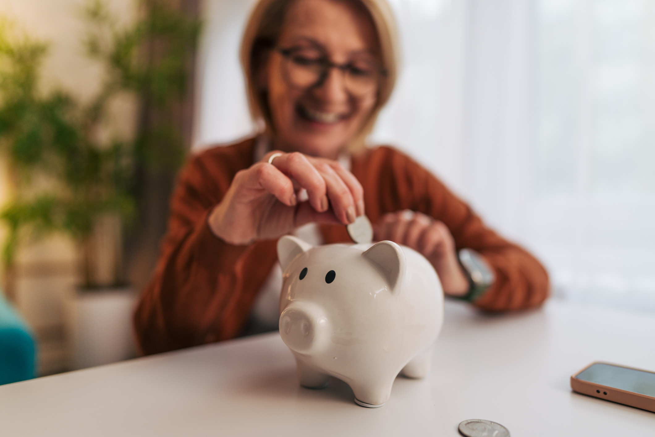 Senior adult woman saving money in piggy bank at home