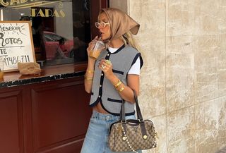 a photo of a woman in front of a coffee shop wearing a vest and jean short outfit that shows the best places to shop for clothes in your 20s