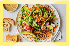 A vibrant salad featuring a mix of seasonal vegetables, including carrots, peas, and greens, served on a white plate with slices of bread on the side.