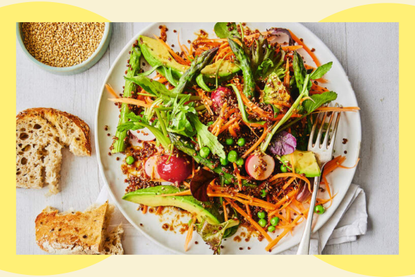 A vibrant salad featuring a mix of seasonal vegetables, including carrots, peas, and greens, served on a white plate with slices of bread on the side.