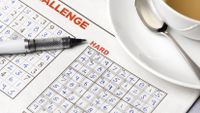 Two sudoku puzzles in a newspaper with a cup of tea and pen