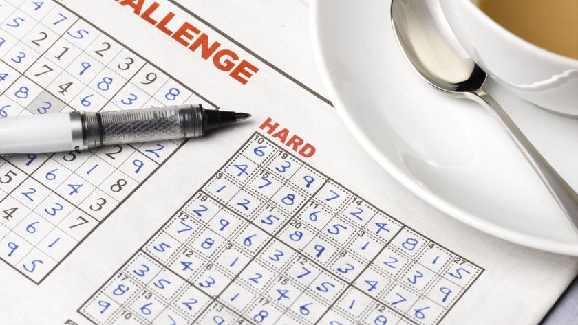 Two sudoku puzzles in a newspaper with a cup of tea and pen