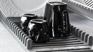 three black mugs upside down on a drying rack