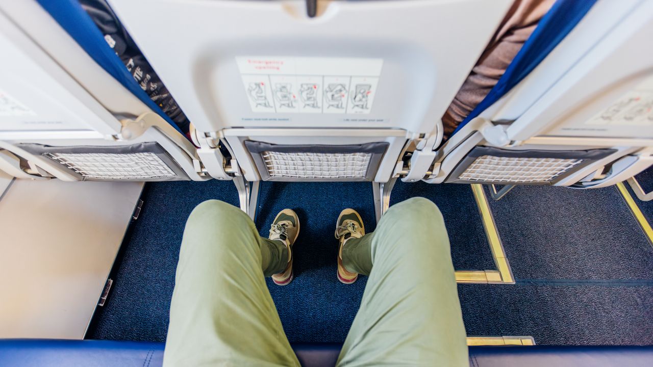 A birdseye view of a person&#039;s legs as they look down at their lap on an aeroplane seat