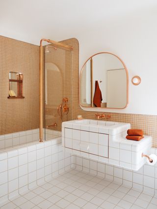 A bathroom with a combined bathtub and shower, a basin, a gold rimmed mirror and white and gold tiles.