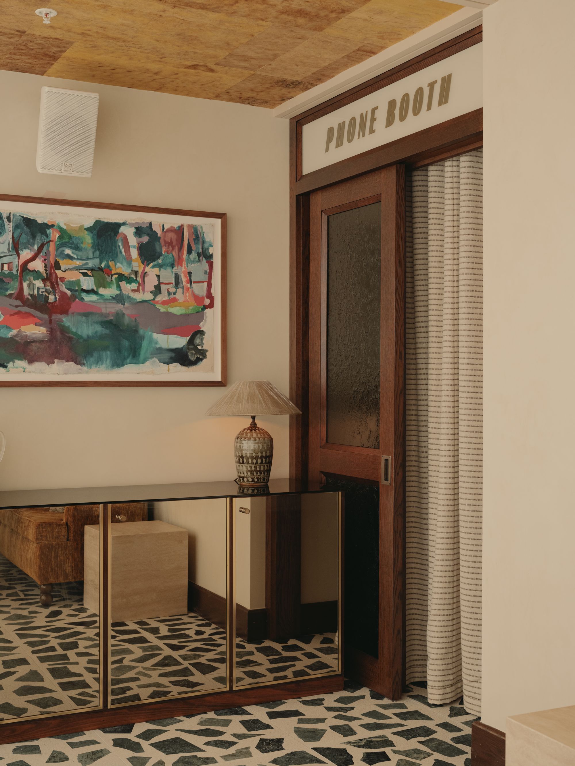 mirrored console at soho house manchester with white walls, timber ceiling, artwork on walll, vintage phone booth with striped curtain, terrazzo floors, and lamp on console