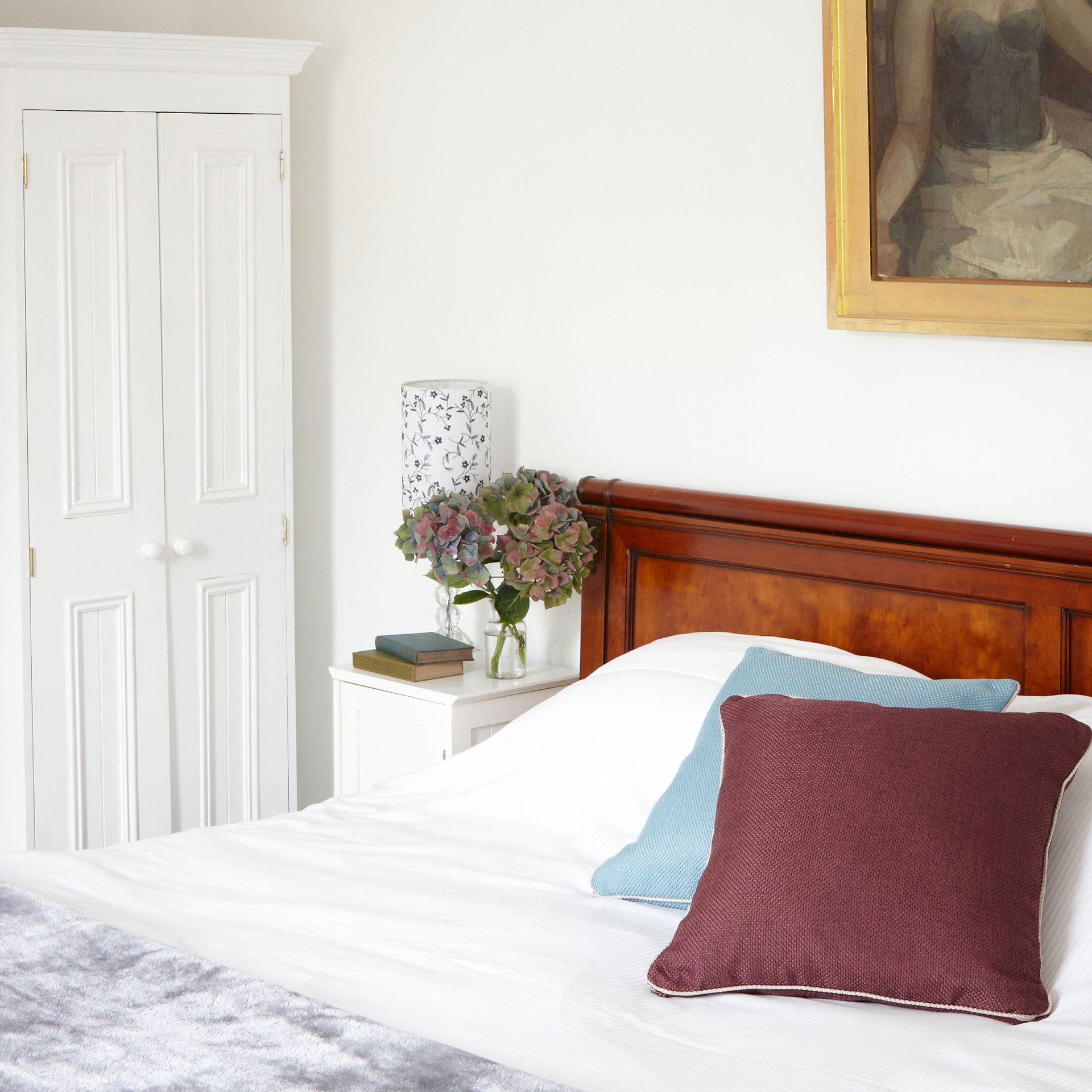 A bedroom with a wooden bed, a painting above the bed and cushions