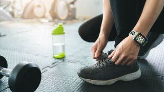 En kvinna med en Apple Watch runt handleden håller på att knyta skorna inne på ett gym.