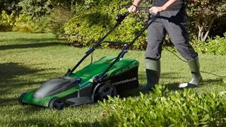 A man pushing a green lawnmower over grass