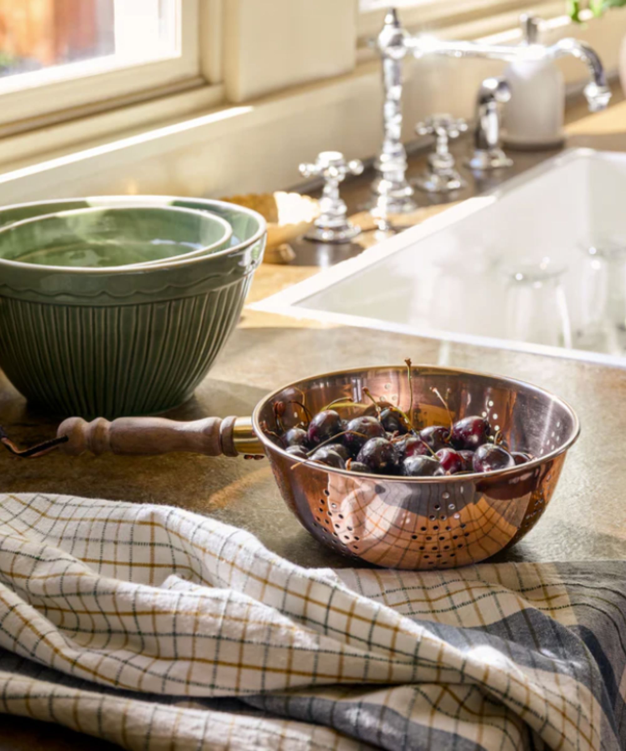 Copper colander filled with cherries next to a kitchen sink