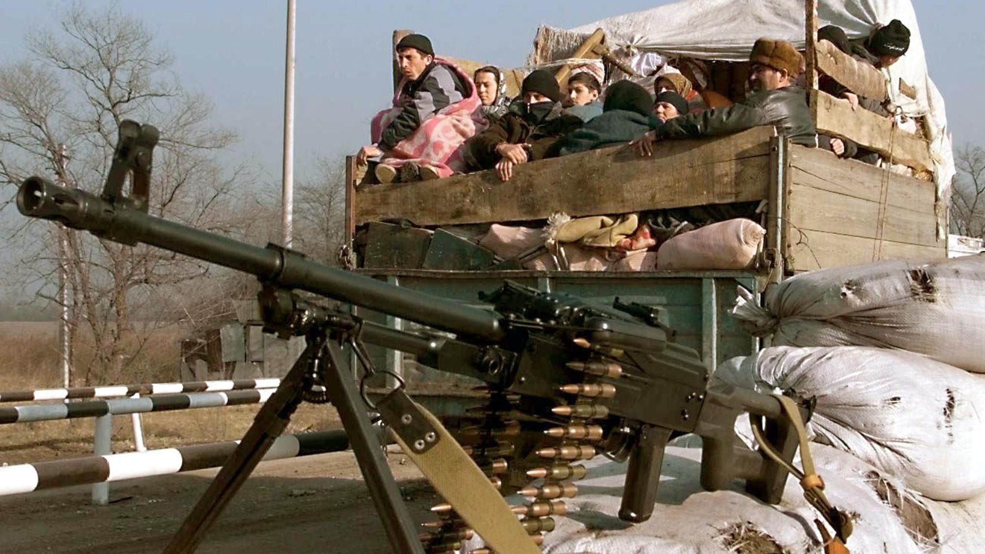 Chechen refugees gathered in the back of an open top truck with a heavy machine gun in the foreground
