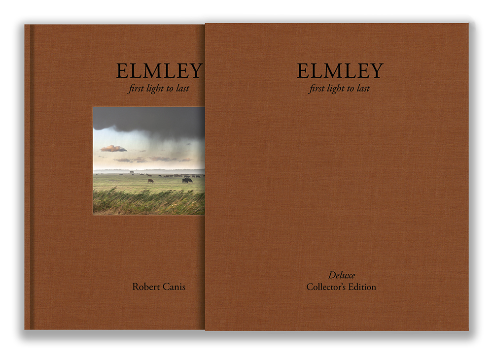 Two rust-brown cloth-bound copies of Elmley: First Light to Last by Robert Canis stand side by side, the left showing a debossed cover image of cattle grazing beneath a storm cloud, the right a plain Deluxe Collector's Edition slipcase.