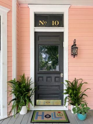 A pink house with two potted ferns and a doormat that reads 'hello'