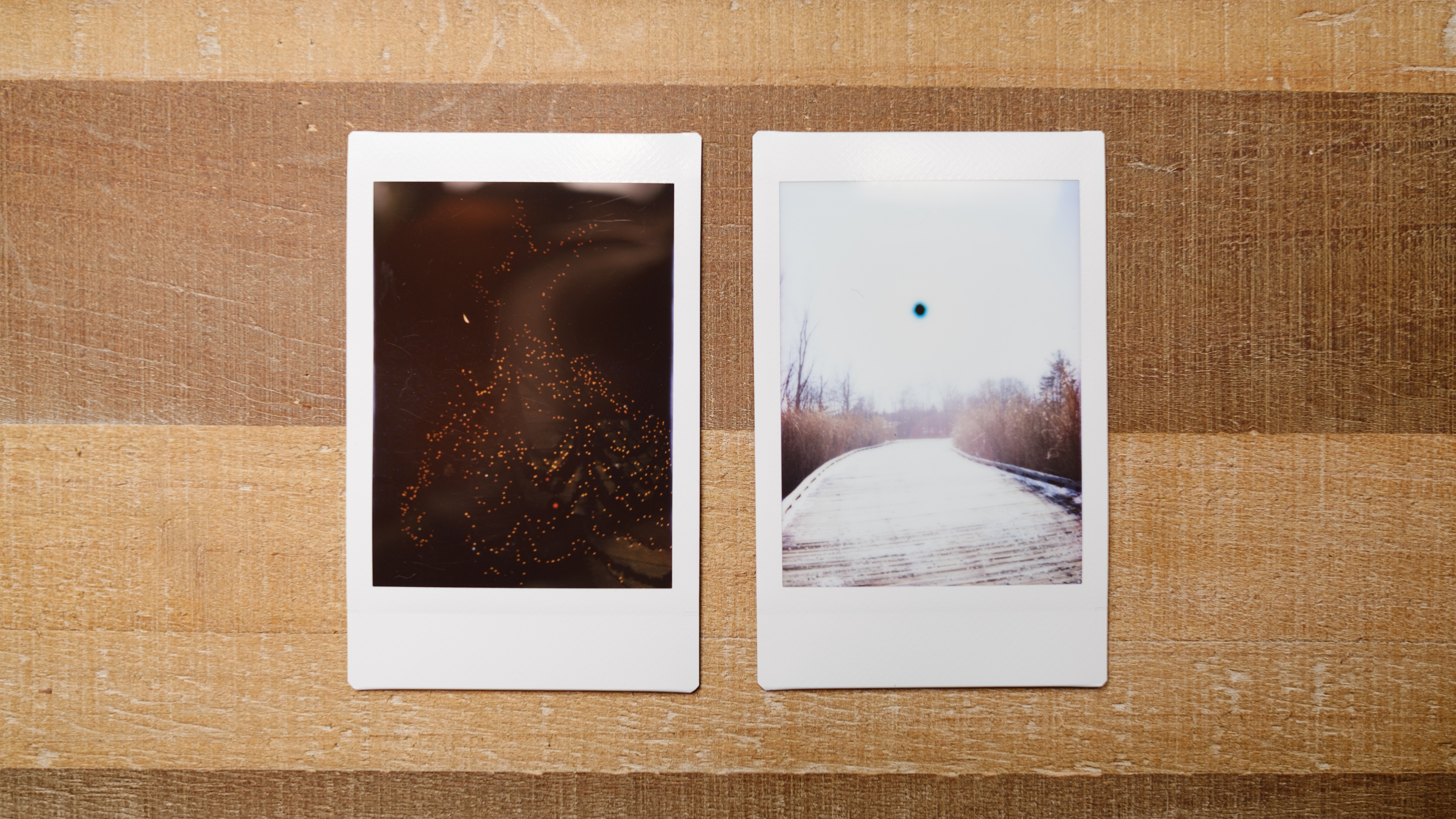 Two images from the Instax Mini SE sit on a table, a dark shot and one with a strange black sun