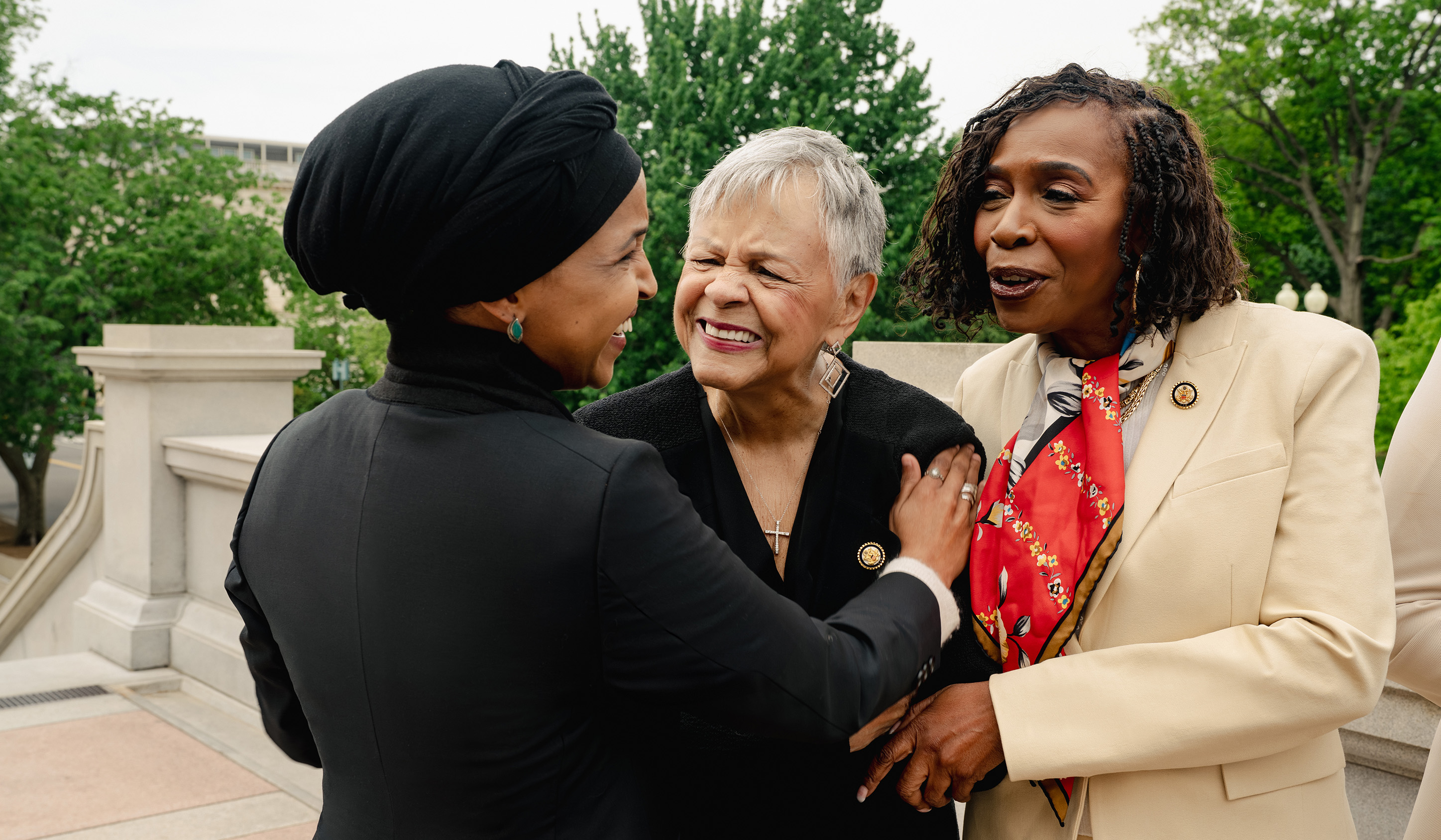 Three congresswomen share a candid moment outdoors on the Capitol grounds, laughing. From left: Ilhan Omar, Bonnie Watson Coleman, and Yvette Clarke.