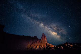 Milky way stretches across the sky diagonally above a large towering rock formation.