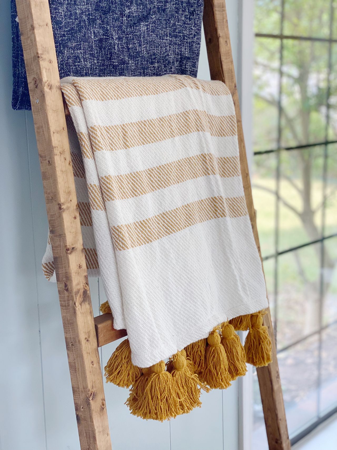 Throw with mustard stripes and pom pom detail hanging on wooden rack