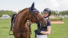 Young girl in competition kit standing with horse