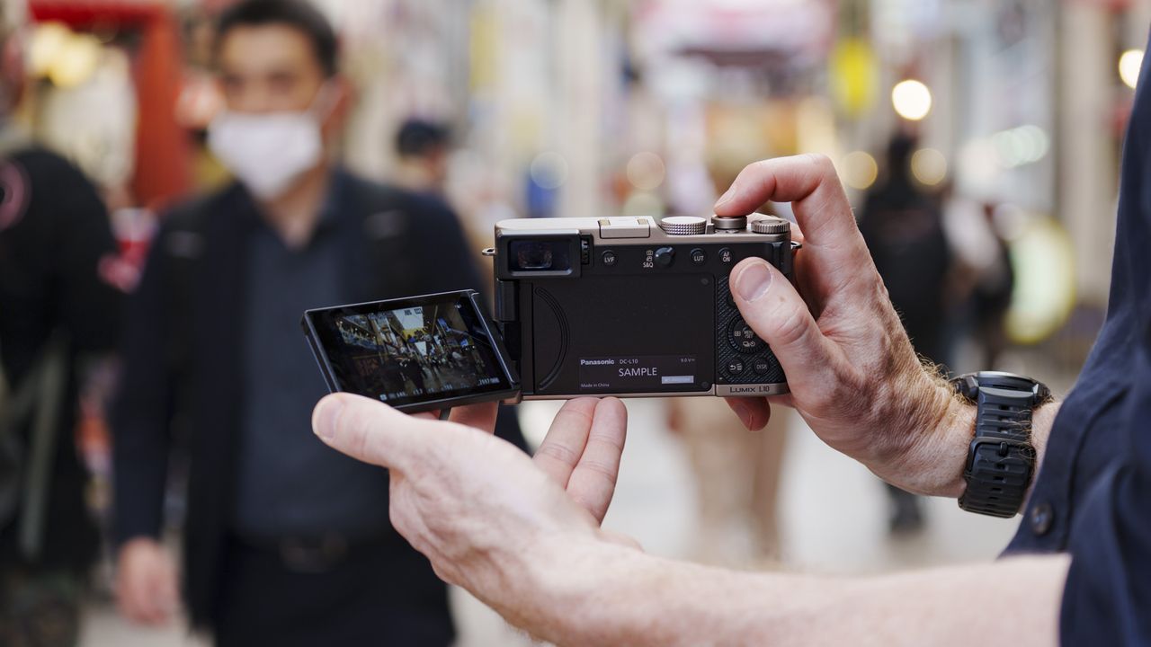 Man holding the Panasonic Lumix L10 compact camera in an urban setting of Japan