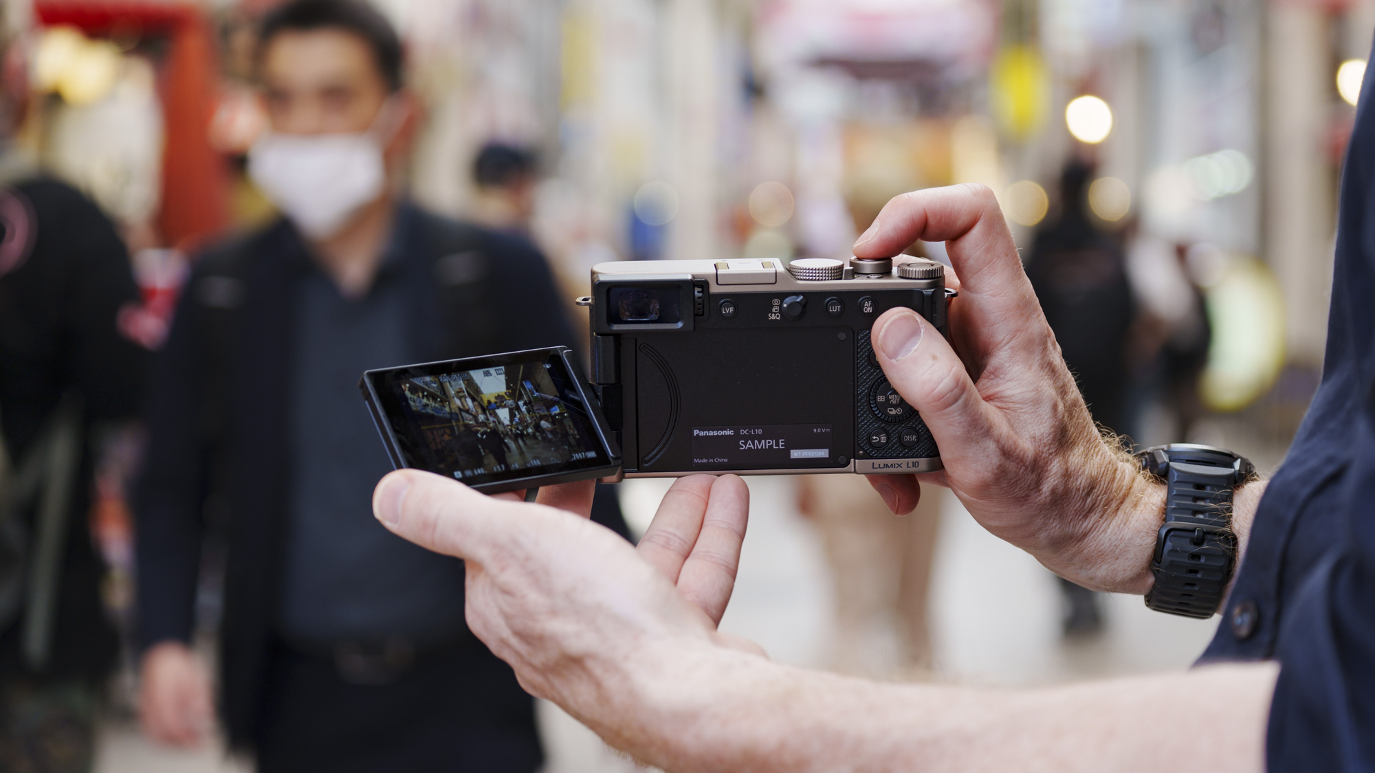 Man holding the Panasonic Lumix L10 compact camera in an urban setting of Japan