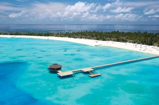 An ariel view of Atmosphere Kanifushi in the Maldives with a long wooden jetty extending out into turquoise blue waters