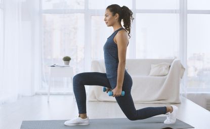 Slim Hispanic girl doing lunges with dumbbells at home, empty space - stock photo