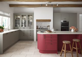 Gray kitchen with red kitchen island, white countertops, bar stools, storage in island, stone floor, beams