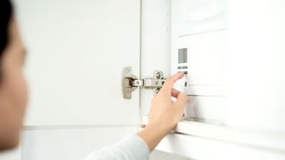 Person adjusting the temperature on a white combi boiler in a white cupboard with door open and metal hinge showing