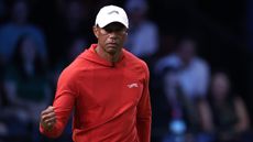 Tiger Woods fist pumps during a TGL match while wearing a white cap and red hoodie