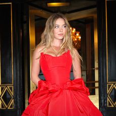 a white woman with long blonde hair wearing a strapless red gown and posing in front of a revolving door