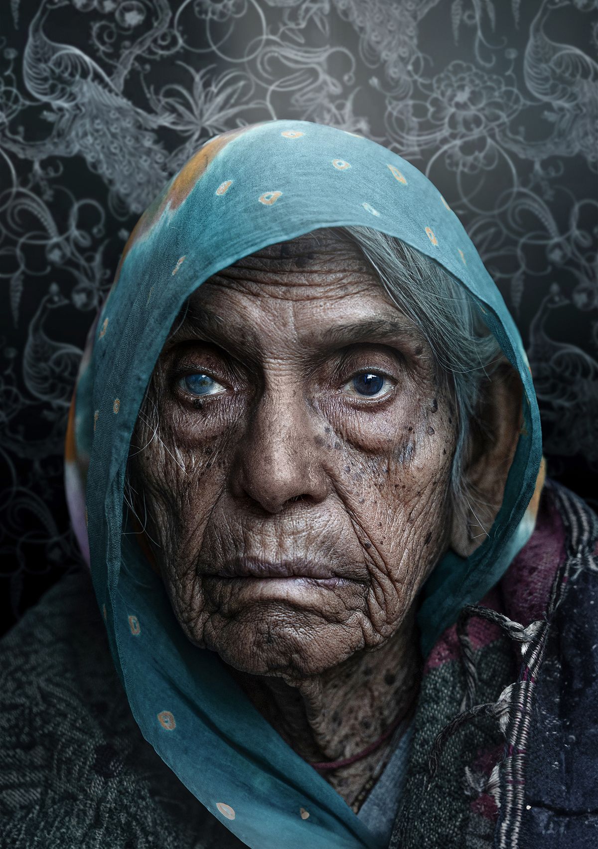 An elderly woman in a patterned scarf and shawl against a dark, floral background, exuding a sense of wisdom and quiet strength