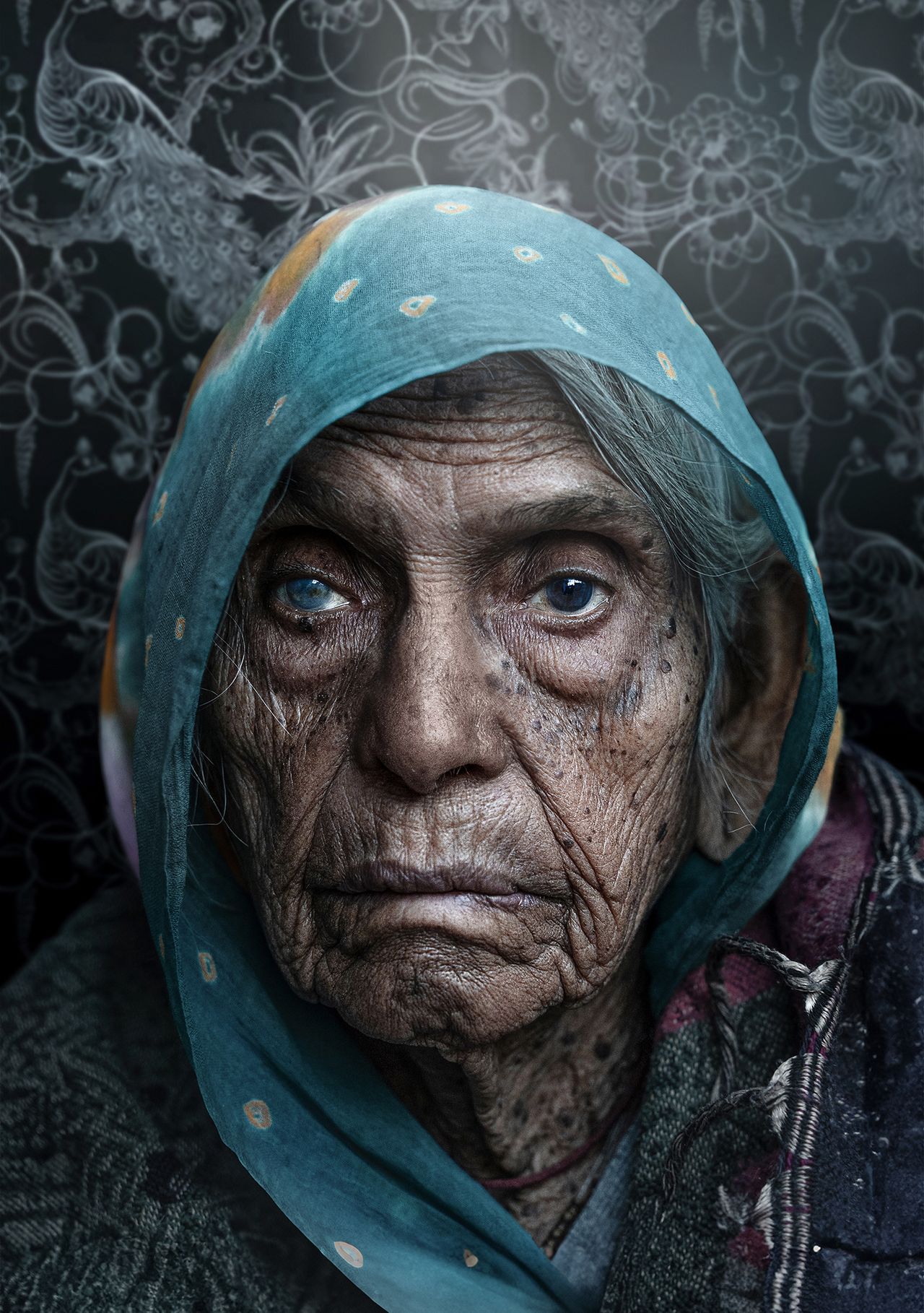 An elderly woman in a patterned scarf and shawl against a dark, floral background, exuding a sense of wisdom and quiet strength