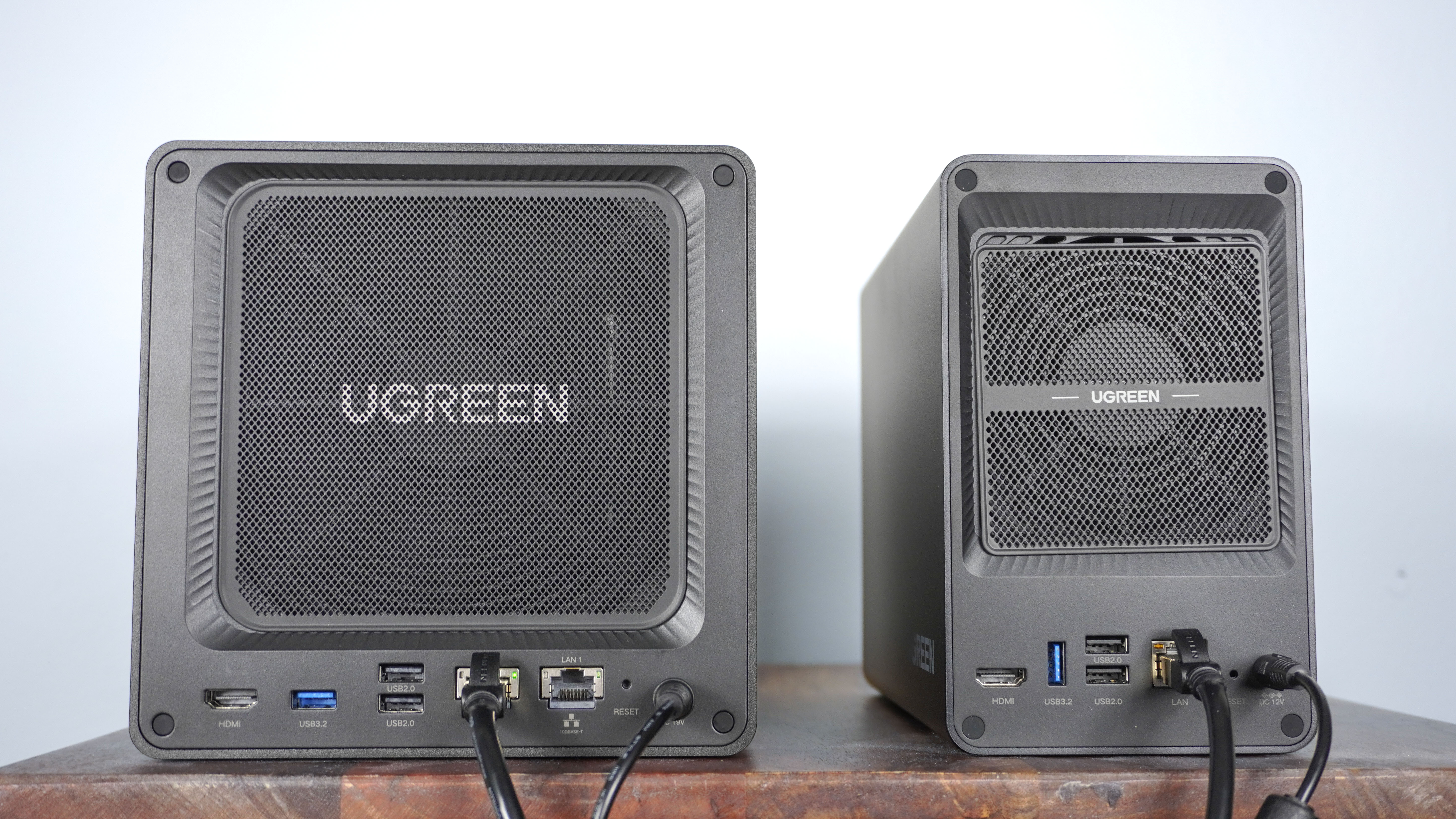 The Ugreen DXP2800 GT and DXP4800 GT side by side and plugged in, seenf rom behind showing off their ports and dust filters